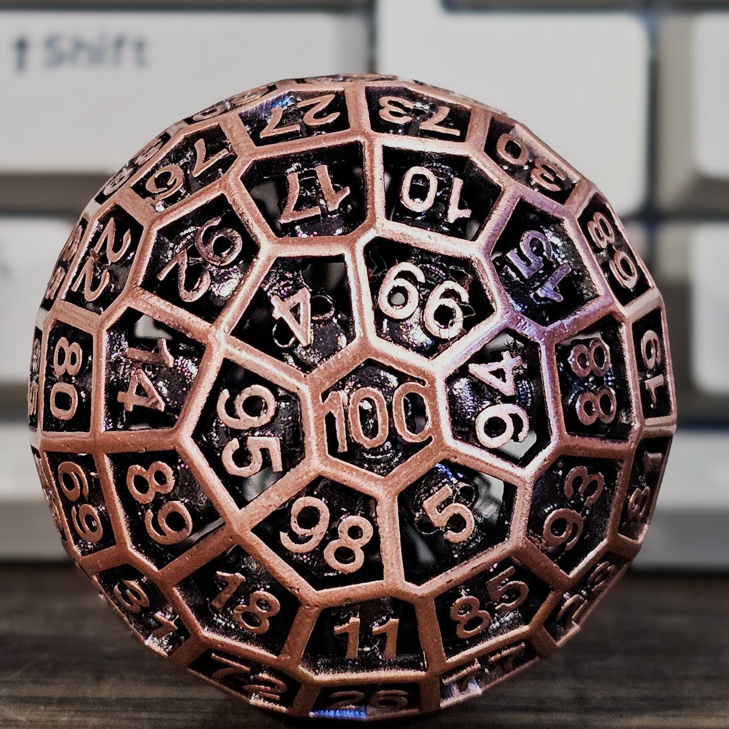 Red Copper Hollow Metal D100 DND Dice with a white mechanical keyboard propped up behind it.