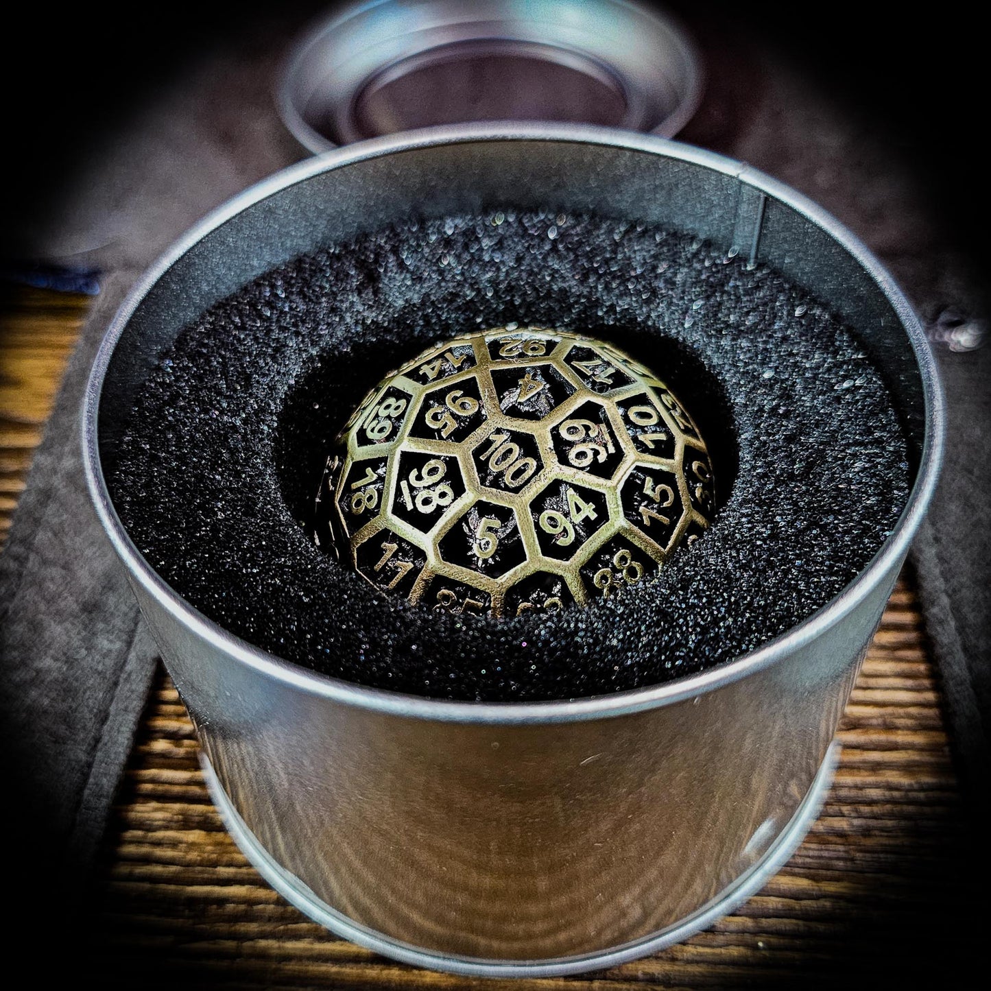 Hollow Metal Ancient Gold D100 DND Dice inside a silver metal container with foam inside to keep the dice protected.