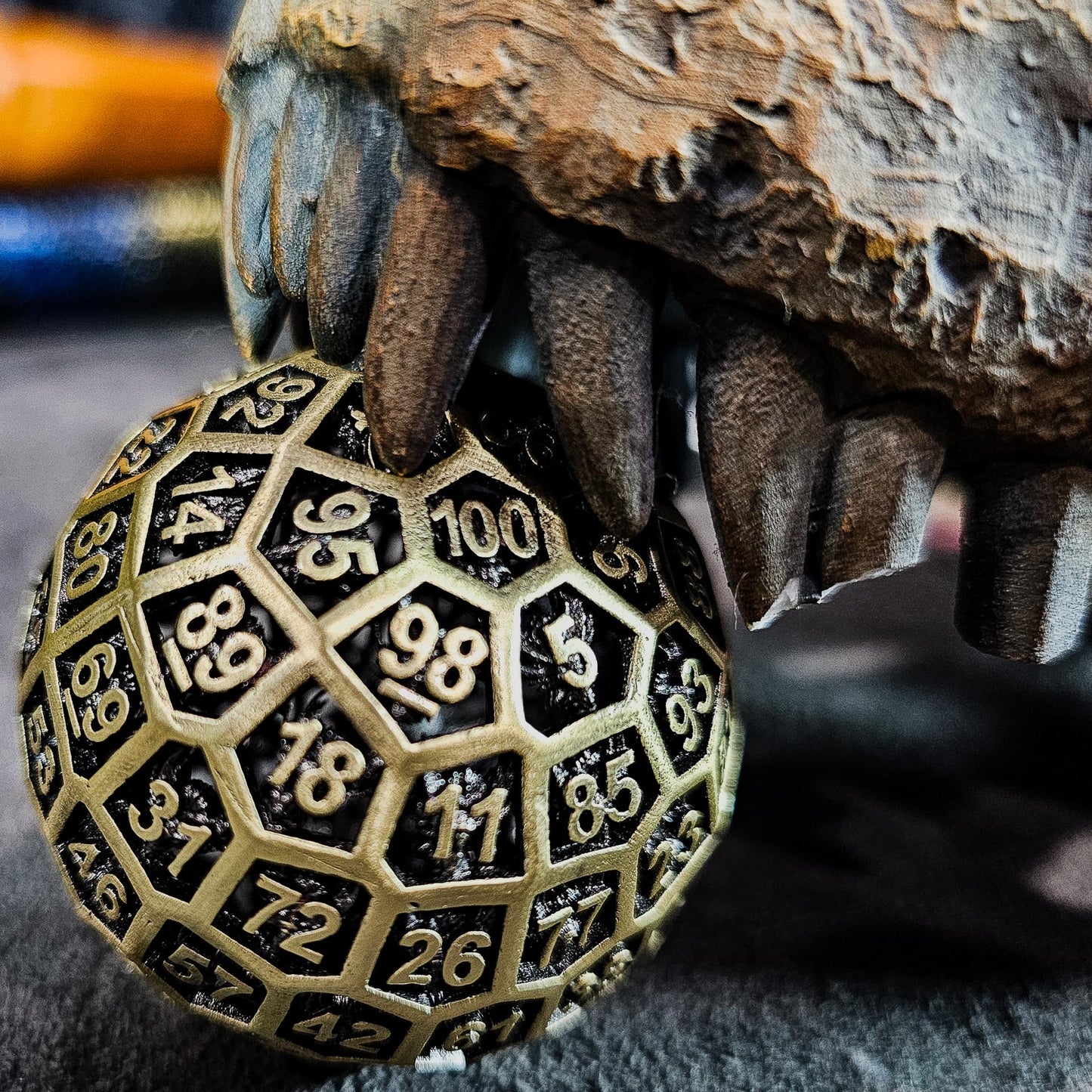 Hollow Metal Ancient Gold D100 DND Dice underneath the teeth of a dinosaur skull.