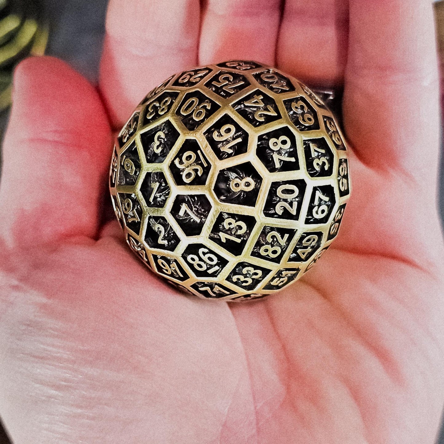 Hollow Metal Ancient Gold D100 DND Dice in the palm of a persons hand