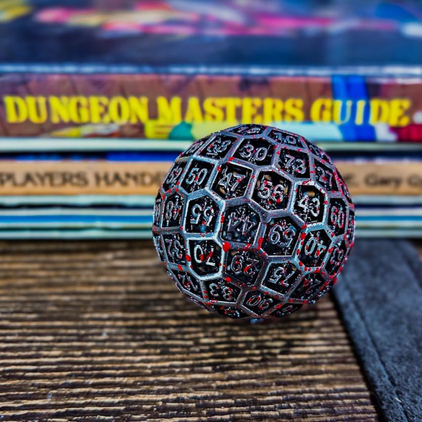 Hollow Metal Silver Blood D100 DND Dice sitting in front of a stack of Dungeon and Dragons Player Handbooks and Guides.