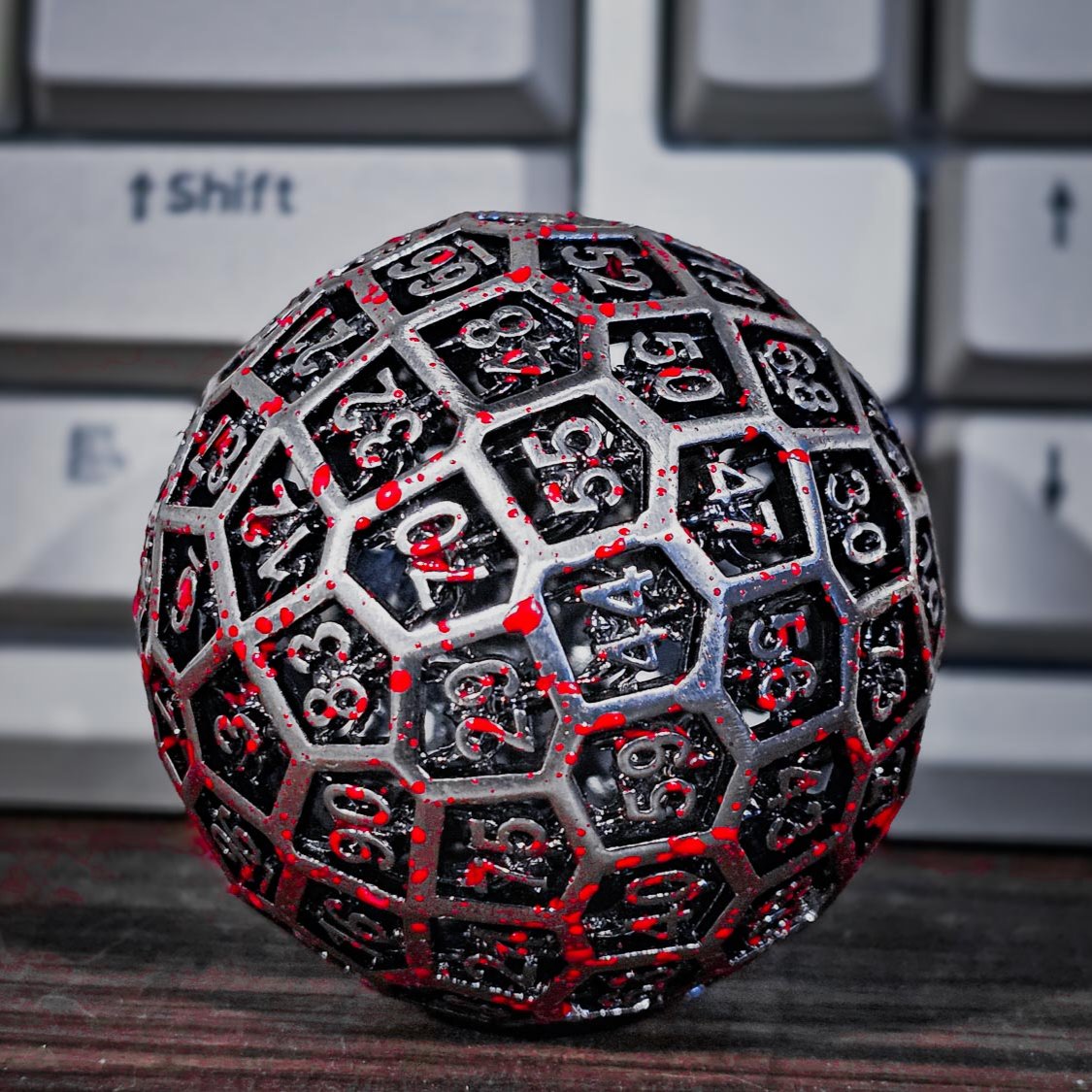Hollow Metal Silver Blood D100 DND Dice in front of a mechanical keyboard in the backdrop.