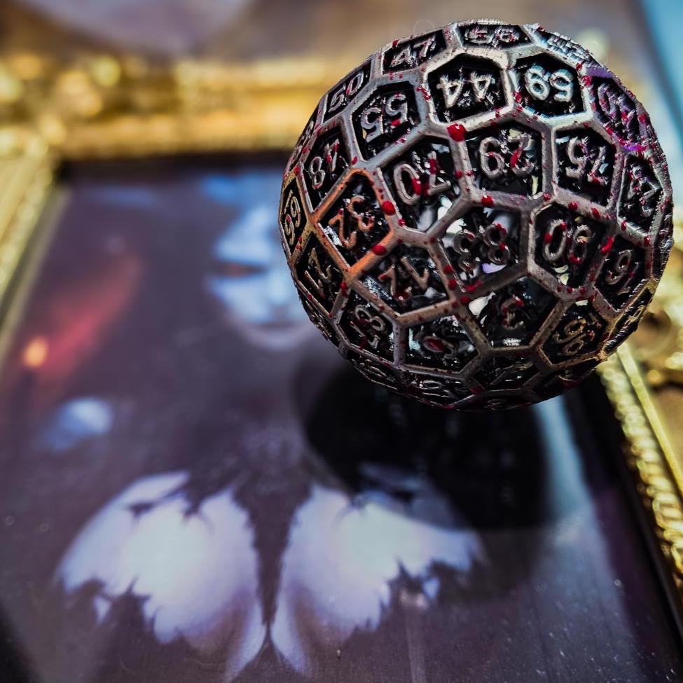 Hollow Metal Silver Blood D100 DND Dice sitting in the corner of a gold picture frame with a large breasted female devil.