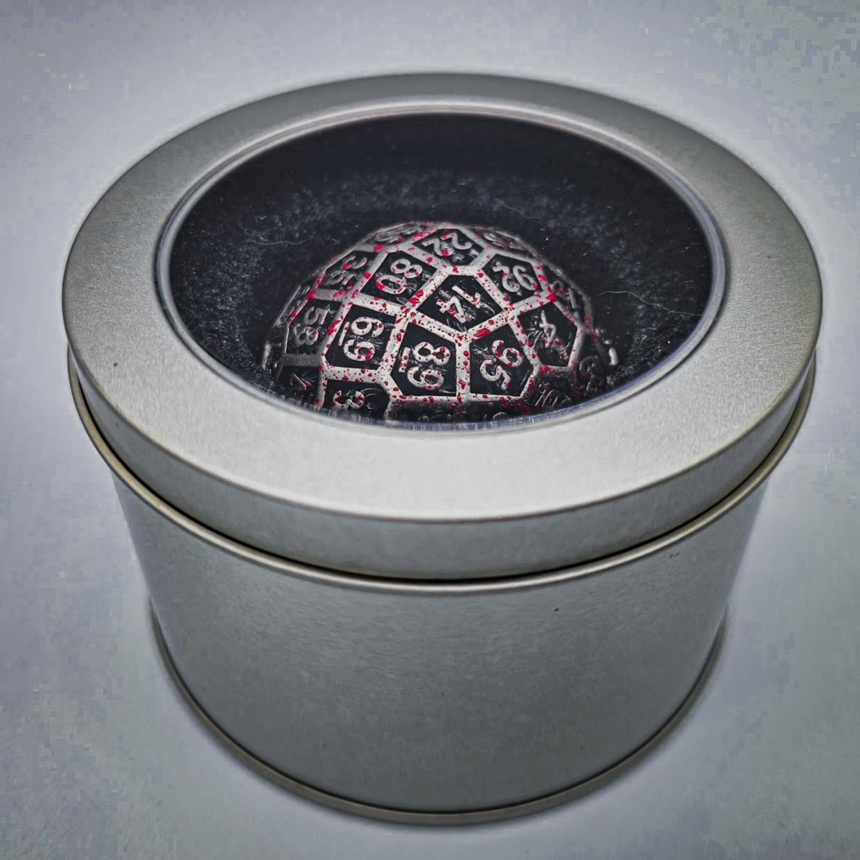 a silver metal container with a plastic see through lid revealing a Hollow Metal Silver Blood D100 DND Dice inside.