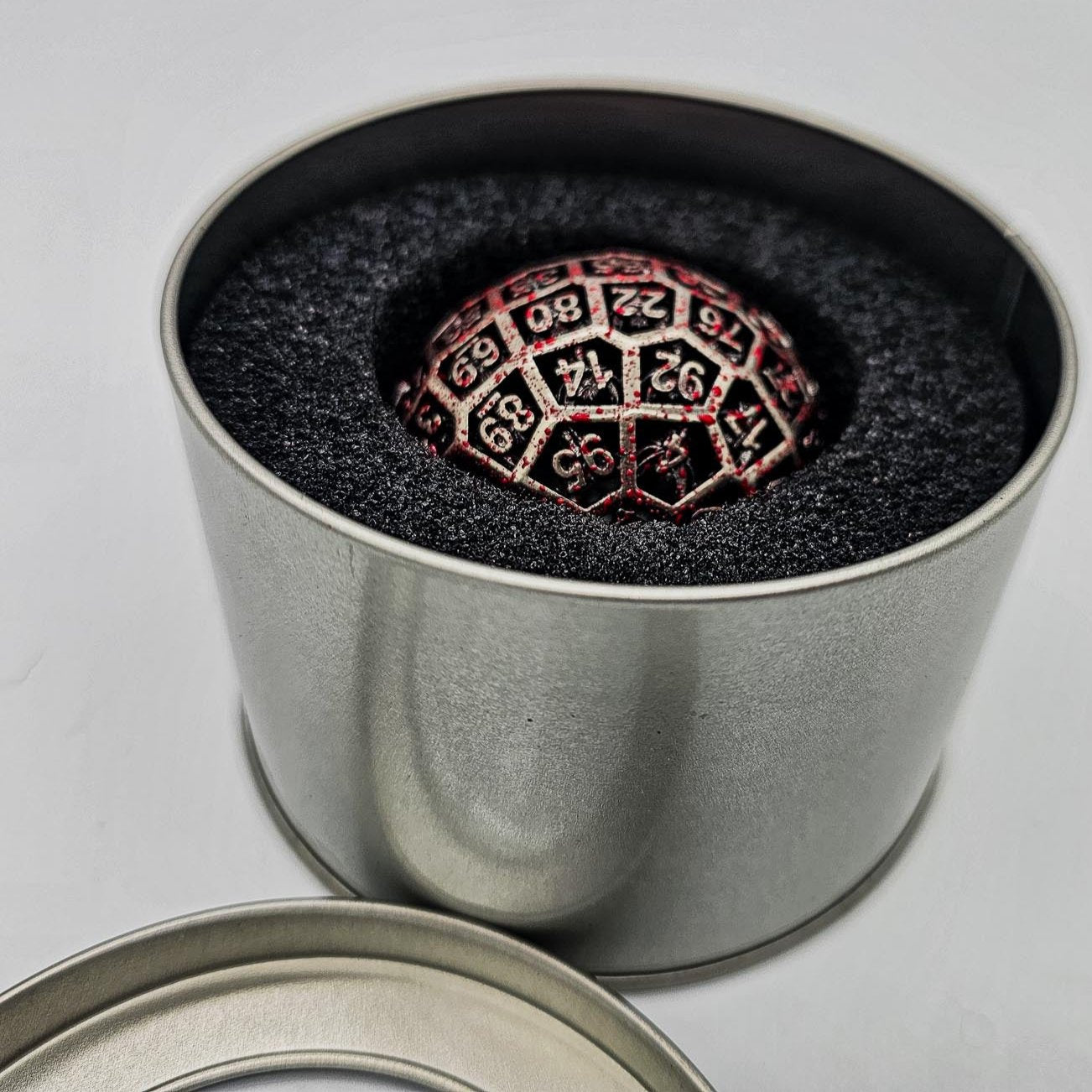 a silver metal container with the lid taken off and placed next to it revealing a Hollow Metal Silver Blood D100 DND Dice inside.