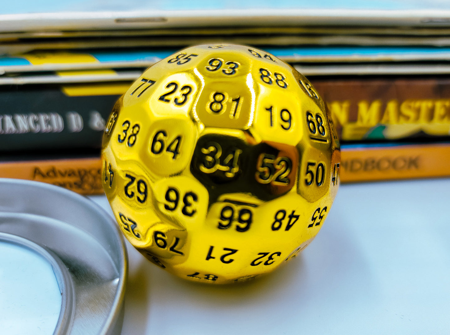 Metal Shiny Gold D100 DND Dice in front of a stack of Dungeons and Dragons booklets.
