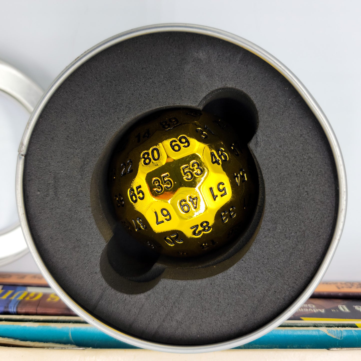 Metal Shiny Gold D100 DND Dice inside it's metal container with the lid off so you can see the foam padding inside to help protect the dice.