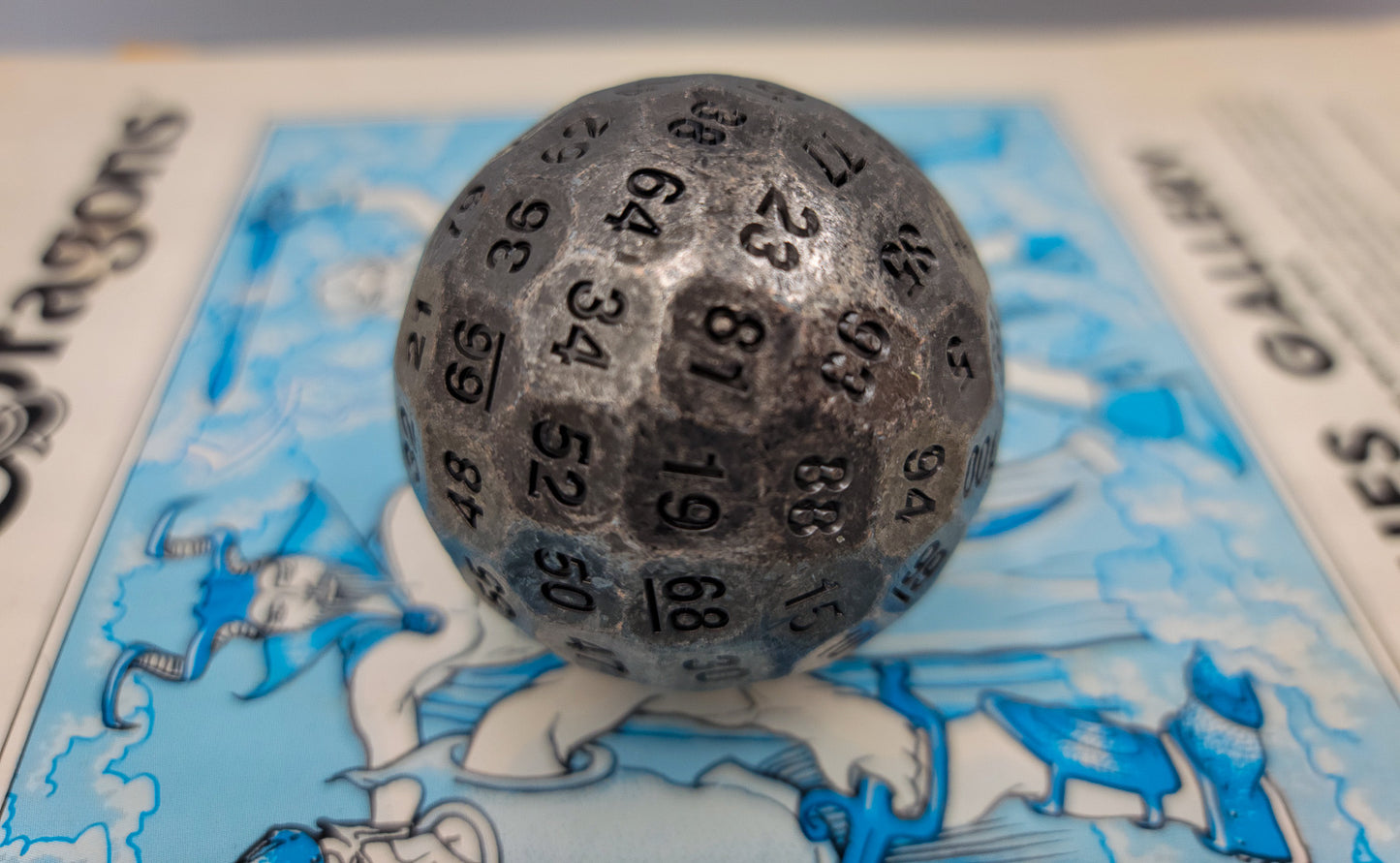 Metal Silver D100 DND Dice sitting on top of a blue Dungeons and Dragons manual.