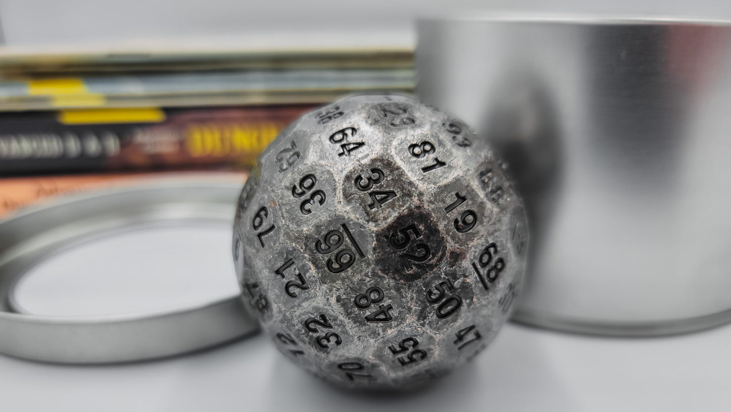 Metal Silver D100 DND Dice sitting between the silver container and lid that has been removed and placed next to the dice. There is a stack of dungeons and dragons manuals behind.