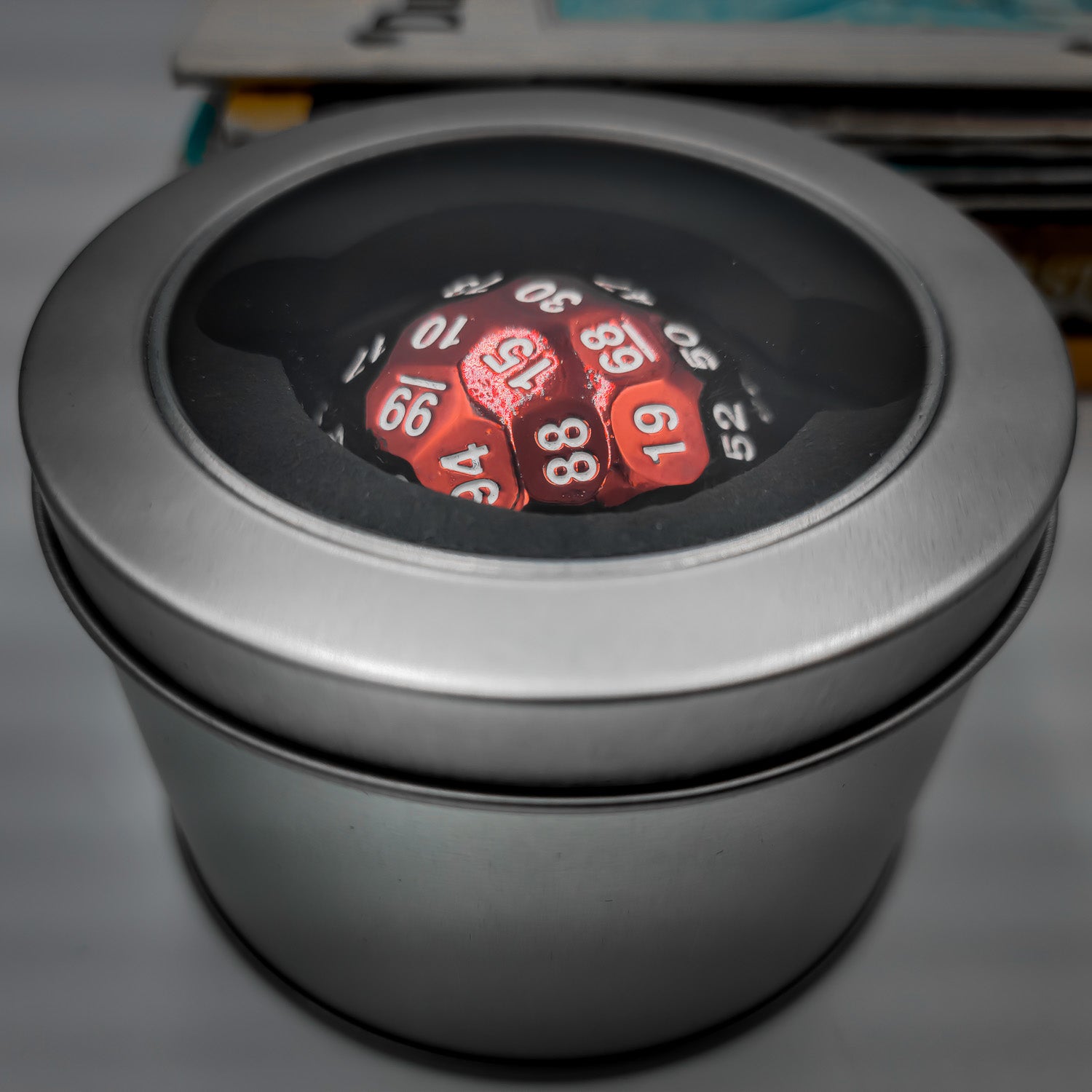 a Red Solid Metal D100 DND Dice inside a silver metal container with a plastic see through lid.