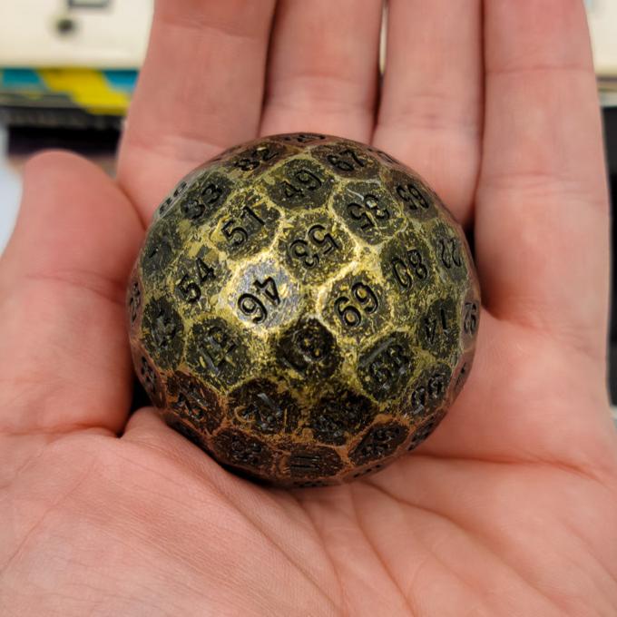 Solid Metal Antique Gold D100 DND Dice in the palm of someones hand.
