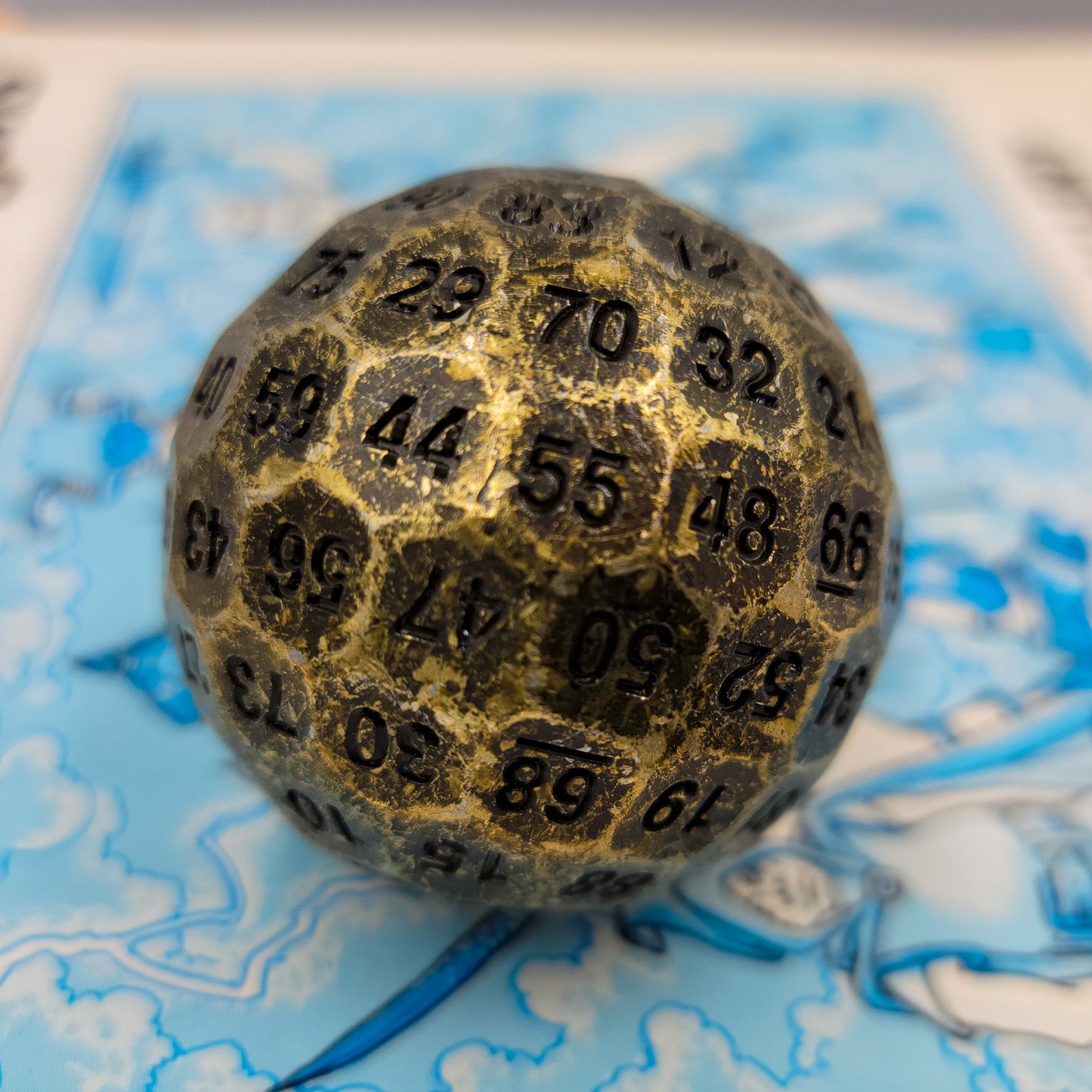 Solid Metal Antique Gold D100 DND Dice on top of a blue Dungeons and Dragons manual.