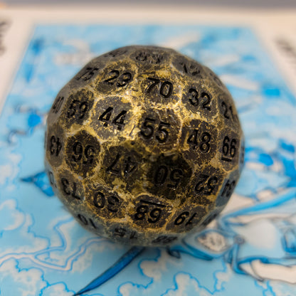 Solid Metal Antique Gold D100 DND Dice on top of a blue Dungeons and Dragons manual.
