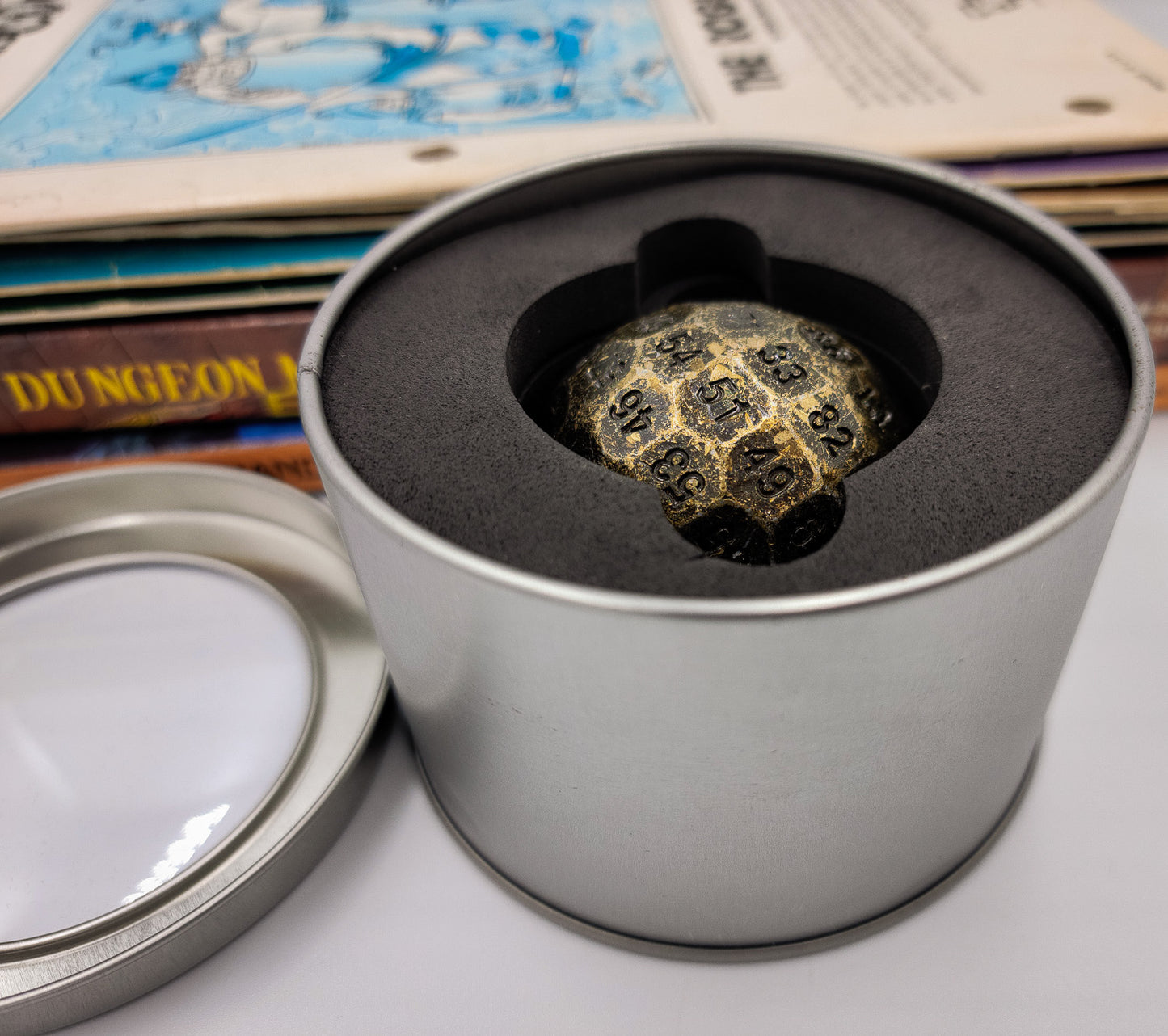 Solid Metal Antique Gold D100 DND Dice inside a silver metal container with the lid off and showing the protective foam padding inside.